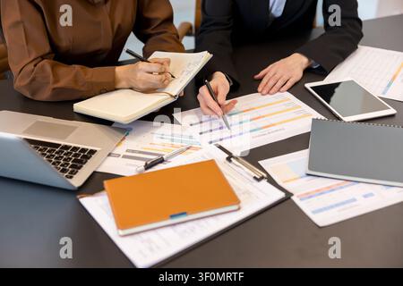Business professionals reviewing financial reports and planning strategy together in an office, working with documents, a laptop, and a digital tablet on a dark table Stock Photo