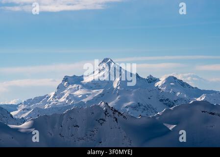 A sharply defined snow-covered mountain summit rises prominently above a layered range of glaciated ridges in the Greater Caucasus, near the Russia-Ge Stock Photo