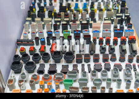 A large display of various colorful automotive and industrial electrical wire harness connectors, plugs, and sockets arranged on a white table. Stock Photo