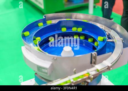 A close-up of an industrial vibratory bowl feeder sorting green plastic bottle caps on a production line, showcasing automated manufacturing and packa Stock Photo