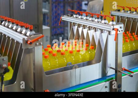 Automated industrial machine sorting plastic bottles filled with yellow liquid and orange caps on a conveyor belt in a modern beverage manufacturing p Stock Photo