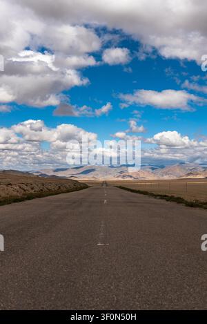 A straight two-lane asphalt road stretches to the horizon across the vast high-altitude steppe of the Pamir Plateau in Gorno-Badakhshan, Tajikistan. Stock Photo