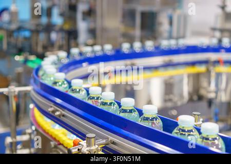 Hundreds of clear plastic bottles filled with fresh drinking water moving along a curved conveyor belt on an automated production line inside a modern Stock Photo