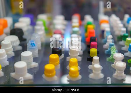 close-up shot of various colorful plastic spout caps and closures used for flexible packaging, neatly arranged in rows on a glass display shelf. Stock Photo