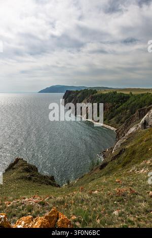 Rugged rocky cliffs draped in conifer forest plunge into the deep blue-green waters of Lake Baikal (Ozero Baykal) along the eastern shoreline of Olkho Stock Photo