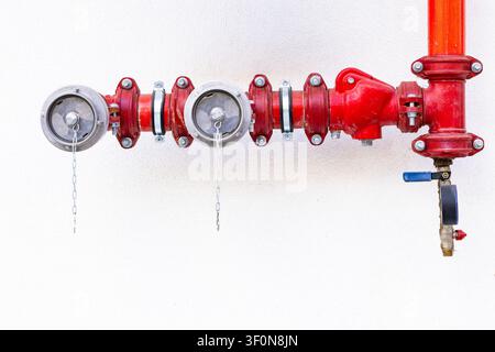Red fire department connection valves and industrial water pipelines installed on clean white building wall exterior Stock Photo