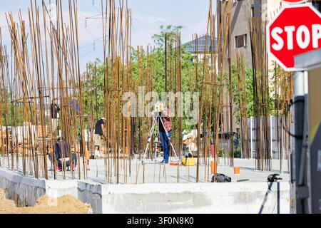 Geodetic engineer and surveyor working with total station at building construction site with concrete foundation and steel reinforcement rebar Stock Photo