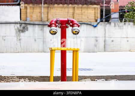 Red fire hydrant department connection stands outside on concrete pavement near construction wall background Stock Photo
