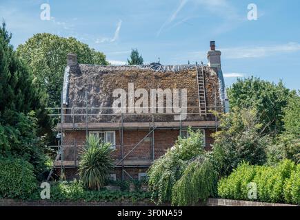 A brick house undergoing a traditional thatched roof replacement or repair in Sidlesham, West Sussex, England, UK. Stock Photo