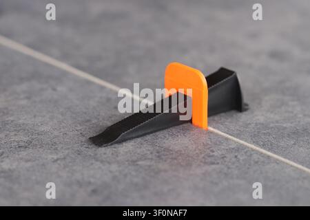 Professional tile leveling system. The process of laying porcelain tiles using a plastic orange clamp and a black wedge to create a perfectly even sea Stock Photo