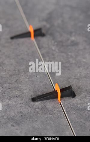 Professional tile leveling system. The process of laying porcelain tiles using a plastic orange clamp and a black wedge to create a perfectly even sea Stock Photo