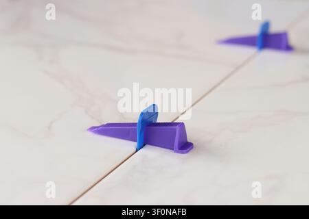 Tile leveling process, tile leveling system, wedge close-up. Purple plastic wedge and blue clip are installed between two marble-textured tiles. Moder Stock Photo