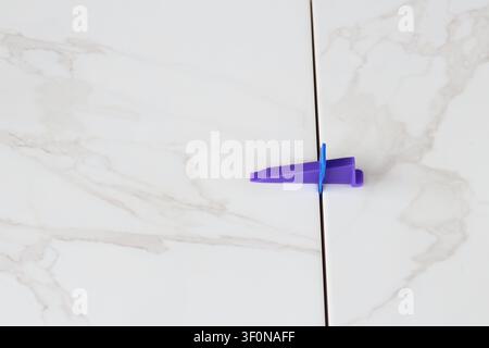 Professional ceramic tile installation. The process of leveling white marble tiles using a plastic wedge and clip. Tile leveling system. Using plastic Stock Photo