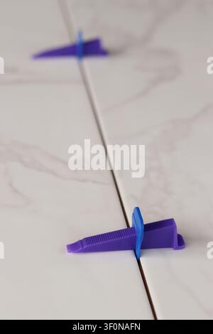 Professional ceramic tile installation. The process of leveling white marble tiles using a plastic wedge and clip. Tile leveling system. Using plastic Stock Photo