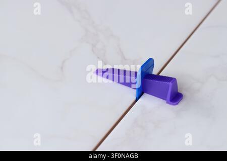 Tile leveling process, tile leveling system, wedge close-up. Purple plastic wedge and blue clip are installed between two marble-textured tiles. Moder Stock Photo