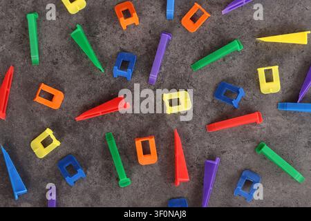 Multicolored plastic clamps and wedges of the tile leveling system on a gray background. Set of bright consumables for construction and repair. Tile l Stock Photo