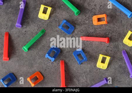 Multicolored plastic clamps and wedges of the tile leveling system on a gray background. Set of bright consumables for construction and repair. Tile l Stock Photo