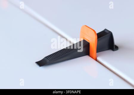 Using a plastic wedge and a clamp of a tile leveling system during repair. Professional laying of ceramic tiles on the floor. The process of leveling Stock Photo