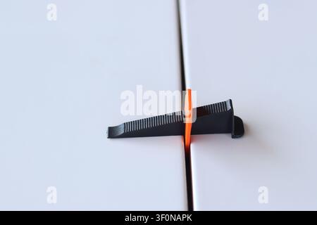 Using a plastic wedge and a clamp of a tile leveling system during repair. Professional laying of ceramic tiles on the floor. The process of leveling Stock Photo