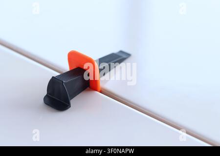 Using a plastic wedge and clamp of a tile leveling system during renovation. Professional laying of ceramic tiles on the floor. The process of levelin Stock Photo