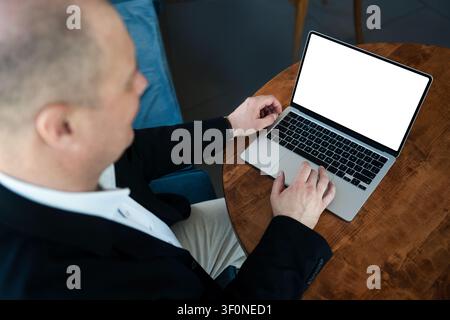 Businessman working on laptop with blank white screen at cafe table. Over shoulder view of business professional using computer for online work, remot Stock Photo