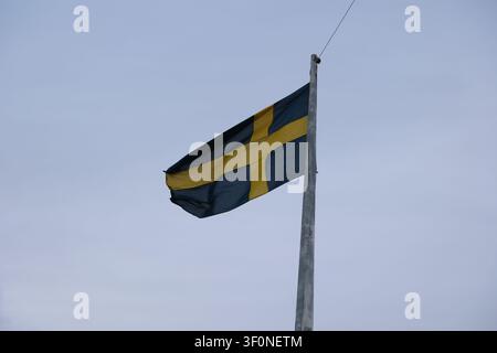 Low angle view of the Swedish national flag waving on a flagpole against an overcast sky. Stock Photo