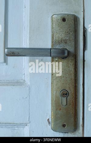 Close up of an old rusty metal door handle and lock with keyhole on a weathered white wooden door. Stock Photo