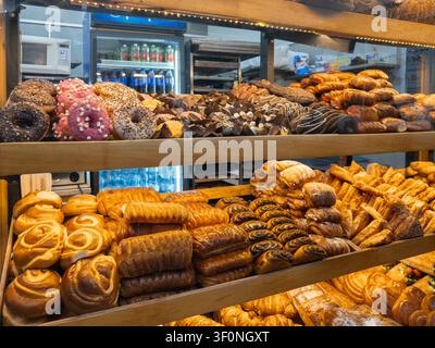 Rows of golden brown breads, sweet rolls, and glazed donuts displayed on shelves in a commercial food store, showcasing tempting treats for customers Stock Photo