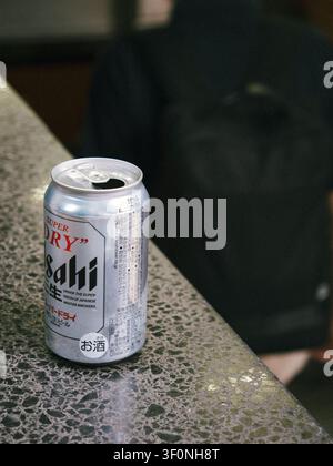 Opened can of Asahi Super Dry beer standing on a stone ledge in Shibuya, Tokyo, Japan, with a blurred backpack in the background Stock Photo