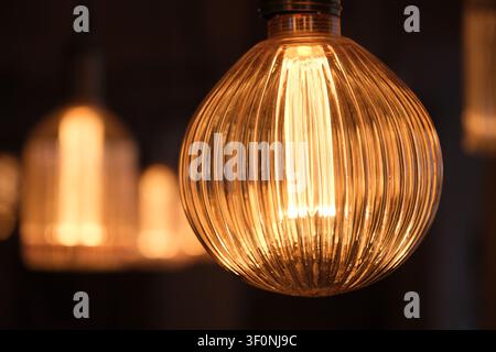 close-up glowing spherical vintage Edison light bulb hanging indoors, emitting a warm, bright light with a soft bokeh background. Stock Photo