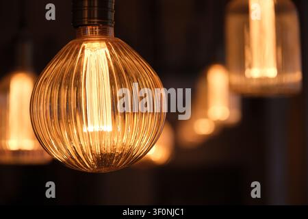 Close-up shot of an illuminated vintage Edison glass light bulb against a dark background. Stock Photo
