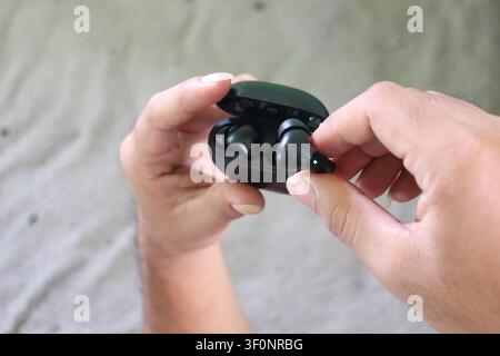 Man Holding Open Charging Case for Black Wireless Earphones, True Wireless Stereo Earbuds with LED Indicator on Textured Background, Modern Audio Cons Stock Photo