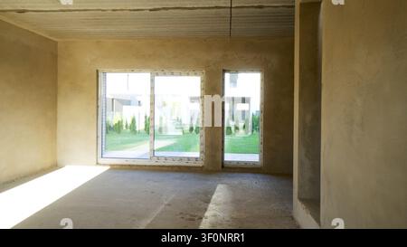 Unfinished room interior in new residential building featuring concrete walls, floor, and large windows opening to a green garden Stock Photo