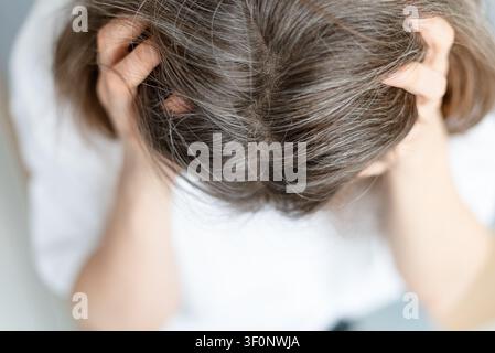 Close up of a woman face showing deep anxiety about her graying hair roots. The mature adult cannot hide distress over visible silver strands. Mother expression reveals inner turmoil and worry. Stock Photo