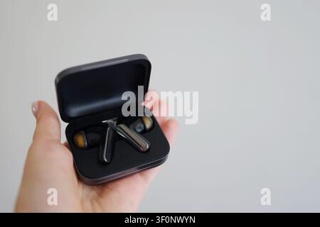 Close-up of true wireless earbuds in an open charging case held in hand against a clean background with copy space. Stock Photo