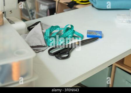 Scissors and measuring tape on a white table with creative chaotic crafting energy indoors. Cutting tool and container arranged with artistic spontaneous casualness on a workbench in closeup. Stock Photo