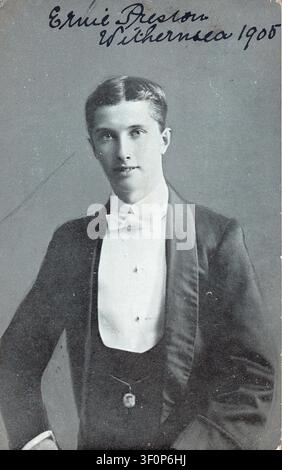 An archival studio portrait captures a dapper young man named Ernie Preston, photographed in Withernsea in 1905. He poses confidently in a formal black tuxedo, complete with a crisp white shirt, wing collar, and neatly tied white bow tie. Believed to be a comedian. From an original postcard published in 1905 by the Yorkshire Gravatone Co. Signed by Preston after a performance in Withernsea, most likely on the pier. Stock Photo