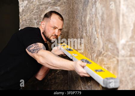 Builder checking the evenness of marble tiles with a level tool, ensuring precision and accuracy during renovation work on a wall Stock Photo