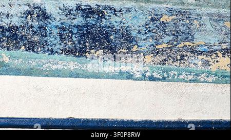 Close-up image of a textured wall with peeling blue and white paint, showing weathered and worn surfaces with layers of colors and rough patterns. Stock Photo