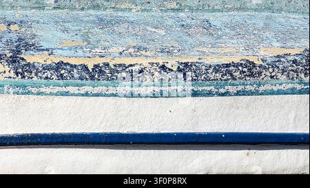 Close-up of a weathered wall featuring peeling blue, white, and beige paint with textured layers and cracks, showcasing rustic and aged surface detail Stock Photo