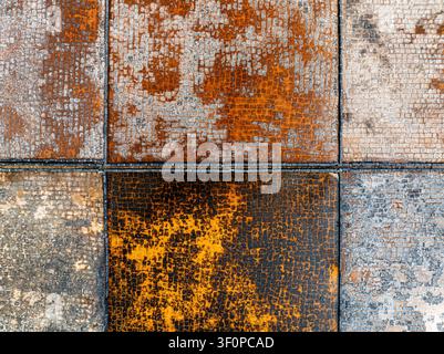 Aerial view of a weathered, grid-patterned surface with rusted metal tiles and textured stone blocks in Mauritius. Stock Photo