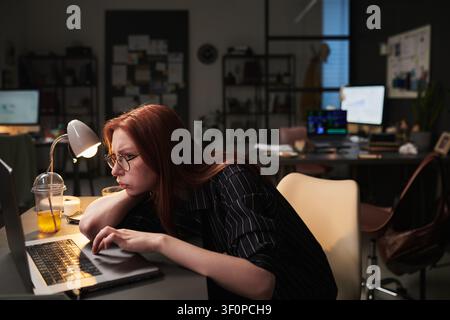 Adult Woman Leaning over Laptop during Exhausting Office Overtime Stock Photo