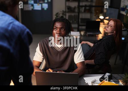Young Adult Black Man Working on Laptop during Late Night Team Meeting Stock Photo