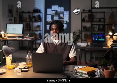 Black Man Working on Laptop in Creative Office at Night Stock Photo