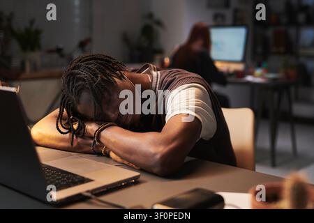 Young Adult Black Male Employee Sleeping at Laptop during Late Night Shift Stock Photo