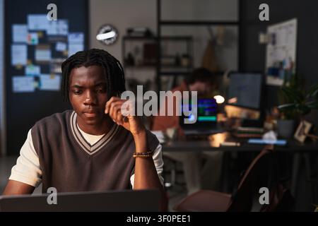 Black Man Working on Laptop in Creative Office at Night Stock Photo