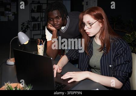 Black Man and Adult Woman Collaborating on Laptop at Night Stock Photo