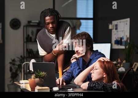 Diverse Coworkers Collaborating on Laptop in Creative Workspace Stock Photo
