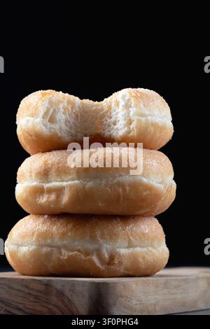 Side view of three delicious ring doughnuts stacked on a rustic wooden surface against a dark background Stock Photo