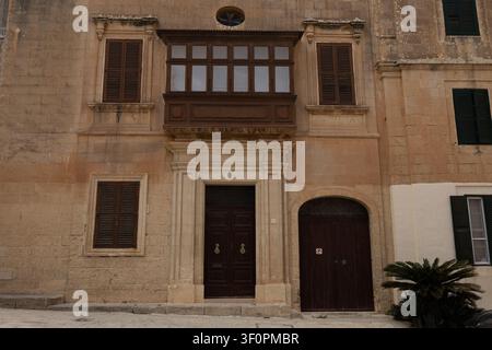 Traditional wooden balcony and shutters on a historic limestone building facade. Stock Photo